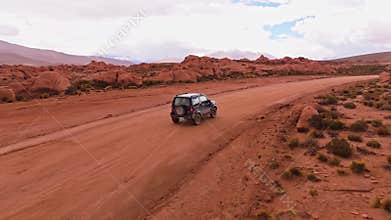 Tracking Shot of a Black SUV Driving Through the Red Rock Desert Landscape of Bolivia, Near a Salt Lake