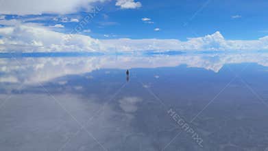 A solitary figure traverses the expansive Salar de Uyuni salt flats in Bolivia, under a clear blue sky