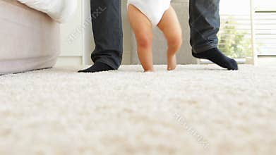 Father helping baby to walk across rug