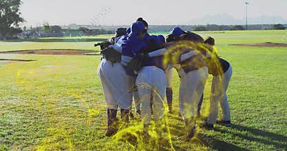 Huddling baseball players linking arms on grassy field near mound, wearing blue jerseys and gloves