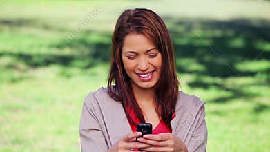 Smiling brunette woman texting on her cellphone