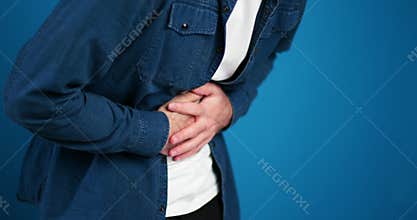 Sick man having stomach pain, spasm selective focus on hands, closeup isolated on blue background