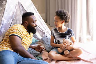African American father and daughter talking in home play corner with star tent and teddy bear