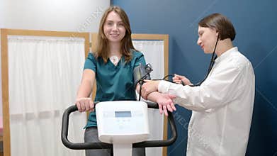 Female doctor cardiologist measures pressure with patient during bicycle exercise for examination cardiovascular system