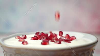 Juicy pomegranate seeds falling into a bowl of creamy yogurt in slow motion, creating a visually appealing and healthy snack