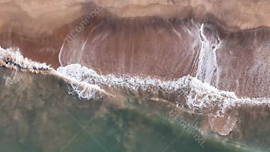 Abstract top-down aerial view of ocean waves breaking on a sandy beach, creating intricate white foam patterns on the shore