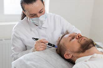 Trichologist doing man improve hair growth procedure, dermapen microneedling, vitamin injections