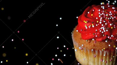 Colourful sprinkles pouring onto cupcake on black surface
