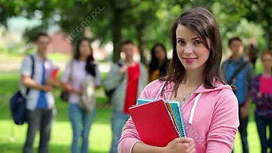 Student smiling at camera with friends standing behind her on grass