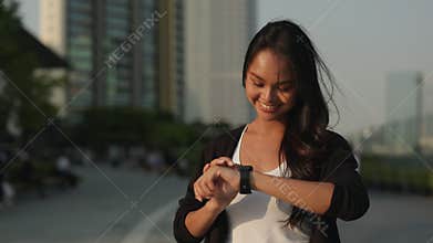 Portrait of Asian woman touches smartwatch screen and stands in urban area