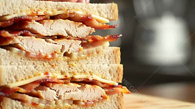 Close-up of hand stacking delicious toasted sandwiches with bacon, chicken, and melted cheese, creating an appealing and tempting