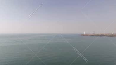 Aerial view of a coastal wind farm with wind turbines generating renewable energy on a cliff by the sea in Devgad, India