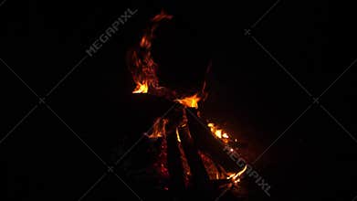 Warm flames flicker in the darkness as logs crackle and burn brightly, creating a cozy atmosphere in the evening air