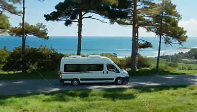 White campervan driving on scenic coastal road with ocean views and lush green trees around it