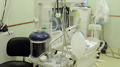 Modern anesthesia machine with various tubes, dials, and a manual resuscitator bag, stands prepared in an operating room