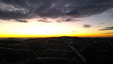 Expansive sunset view over rolling hills, showcasing vibrant orange and yellow hues illuminating the sky, with gradual camera