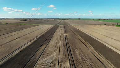 Aerial view of cultivated farmland showing soil patterns under a blue sky with scattered clouds
