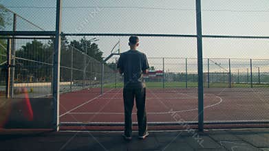Teen stands still at sunrise outside chainlink court fence