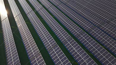 Aerial shot shows an expansive solar farm. Rows of panels are neatly arranged on green grass
