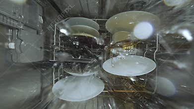 Inside view of a running dishwasher with water spraying over dishes and utensils, creating a dynamic underwater-like perspective