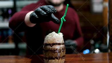 A bartender sticks a green plastic straw into a chocolate-coffee drink with cream