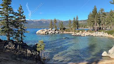 Wide scenic view of Sand Harbor beach cove with emerald water and pine forest background