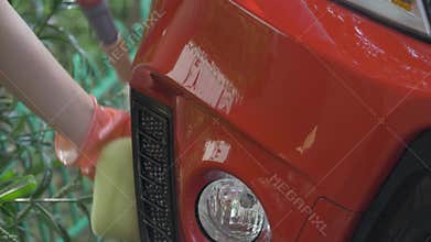 Hand wipes dirt from red car with yellow sponge