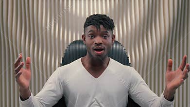 Excited African American cyber man say wow feeling shock sitting in chair in futuristic studio stunned male gamer guy in