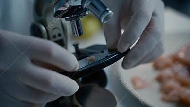Scientist in gloves uses tweezers to place a raw meat sample on a glass slide, then puts it under a microscope for