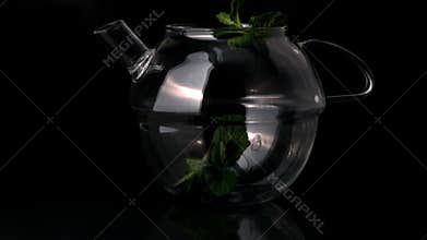 Mint leaves falling into glass teapot