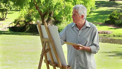 Serious mature man painting on a canvas
