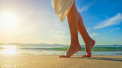 Young woman in white dress walking alone on the beach in the sun