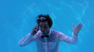 Businessman underwater in swimming pool talking on smartphone