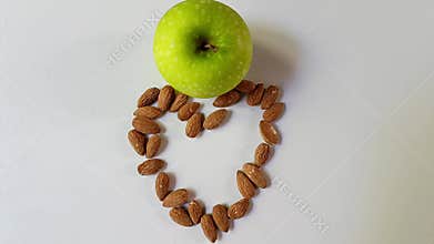 Green apple above heart shape made of almonds on white background