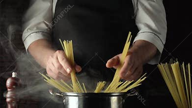 Chef prepares spaghetti by placing uncooked pasta into a pot of boiling water, steam rising, with ingredients and utensils visible