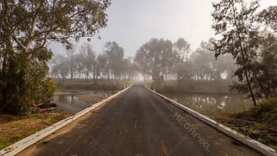 A road bridge crosses a border river and fog shrouds gum trees on the far bank.
