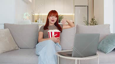 Young woman with popcorn watches movie trailer on laptop laughs out loud enjoys fun teaser and cheer