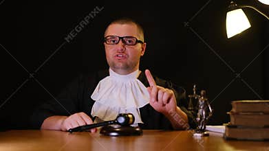 Angry male judge pointing finger and hitting gavel in courtroom