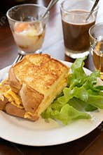 Toasted egg sandwich with fresh lettuce on plate and coffee in background, cozy breakfast scene with warm light
