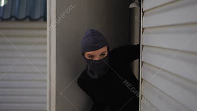Masked girl burglar sneaking through garage entrance into household
