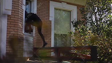 An Intruder Is Stealthily Entering a House Through a Window in Middle of the Day