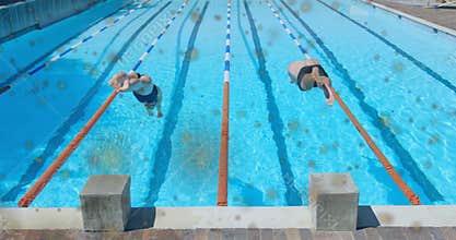 Two swimmers crouching on blocks diving into pool splashing then calming water for sports event
