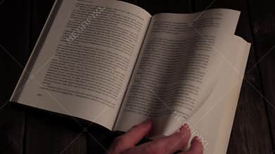 Hand turning pages of an open book on a wooden table