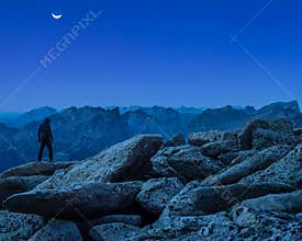 Lone explorer at night stands on the edge of the steep and high mountain