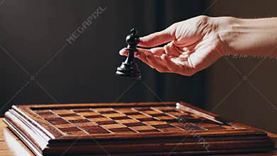 Enigmatic hand belonging to a man is causing a black wooden chess bishop to magically hover and float above a classic chessboard