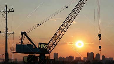 Construction crane silhouette against a vibrant sunset with city skyline in the background