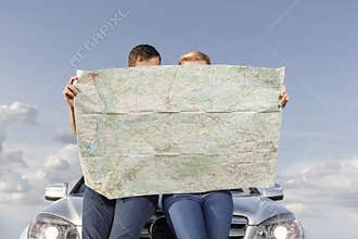 Couple reading map while leaning on car hood during road trip
