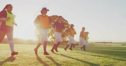 Running seven softball players warming up on softball field in low sun, wearing pinnies and cleats