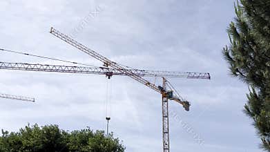 Tower crane above treetops, metal structure, blue sky background