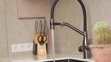 Modern kitchen faucet in action with flowing water near utensils